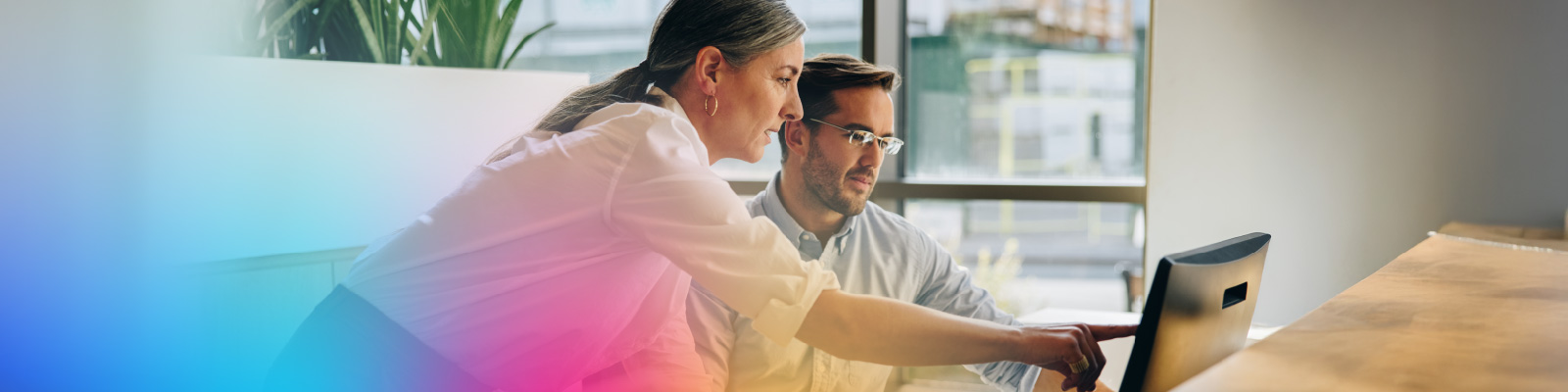 Two colleagues collaborating and pointing at a computer screen in a modern office setting.