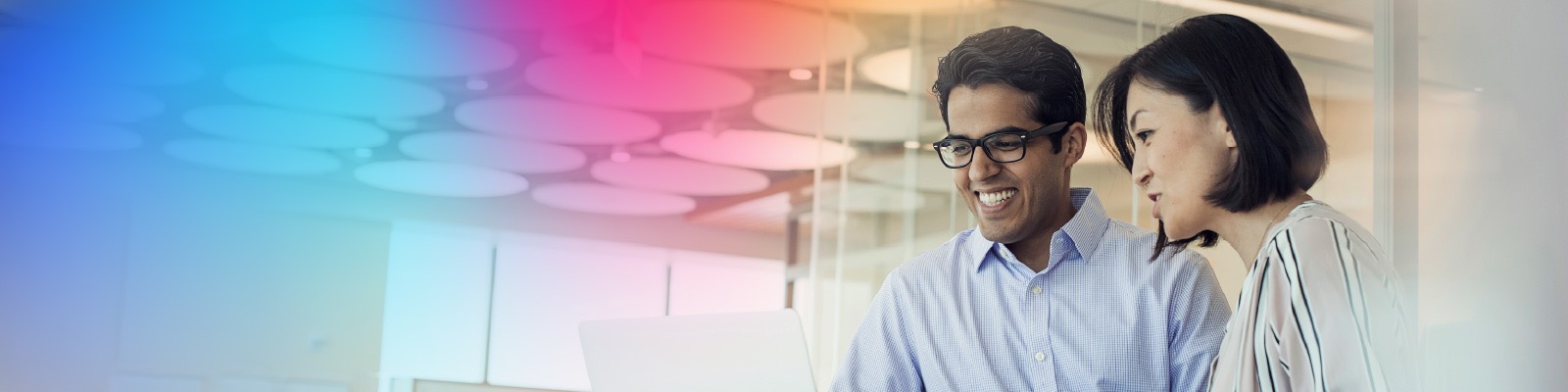 Two colleagues looking at their computers, smiling, collaborating together.