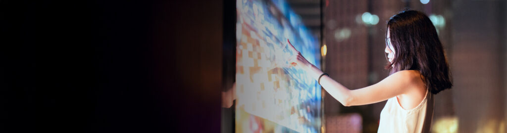 A person looking and interacting with a touchscreen in a dimly lit room.